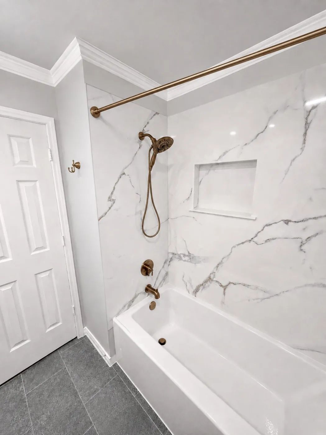 Bathtub replacement with stone-look surround, recessed niche, champagne bronze Delta fixtures, gray flooring and fresh paint