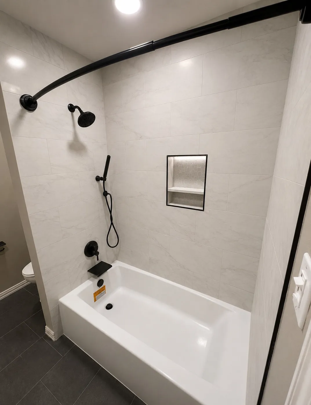 Bathtub replacement with light tile surround, recessed niche, matte black shower system, curved shower rod and dark flooring