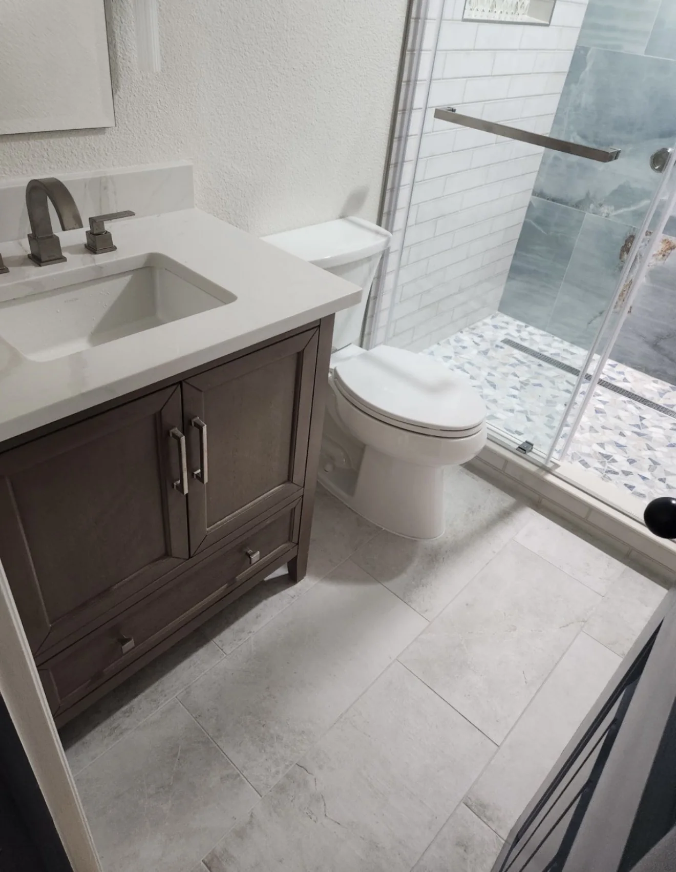 Replacement vanity with quartz countertop and ivory bathroom flooring beside the remodeled shower