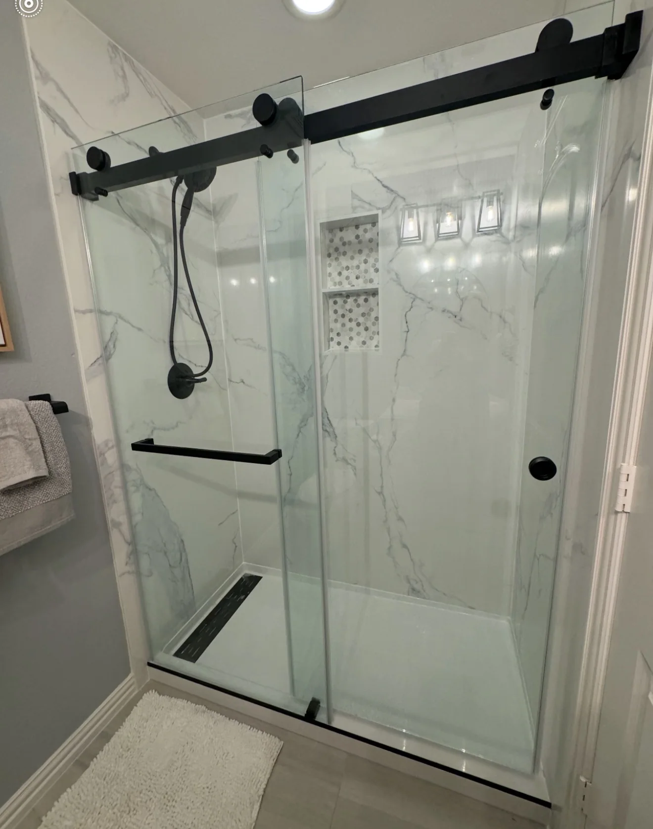 Guest bathroom tub-to-shower conversion with marble-look walls, black farmhouse sliding glass and custom niches