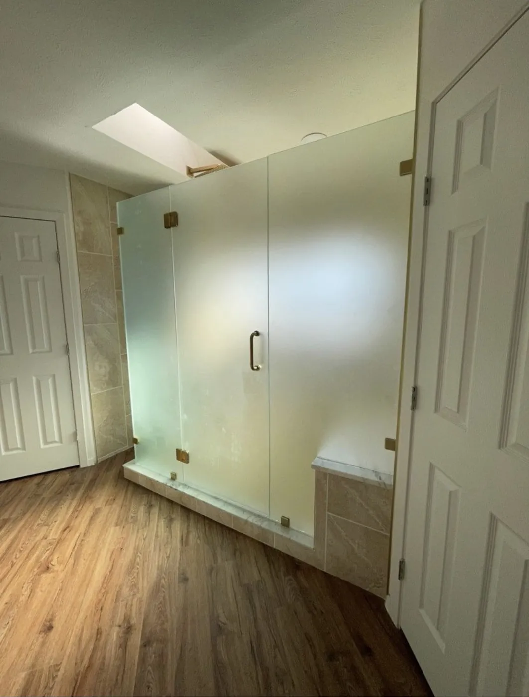 Shower remodel with custom obscure privacy glass, brushed bronze hardware, stone-look tile, built-in bench and wood-look flooring