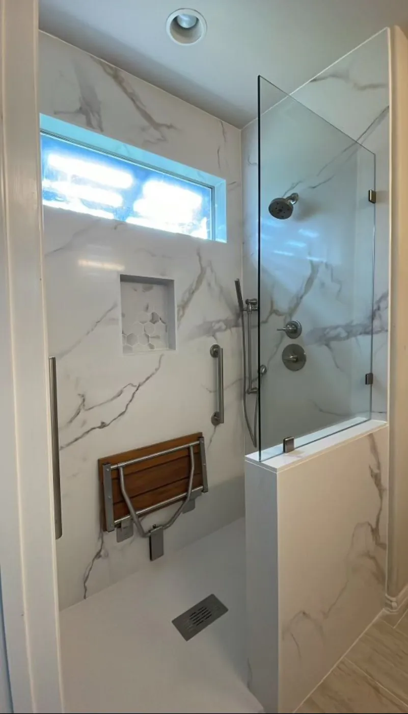 Zero-entry accessible shower with fold-down wall seat, grab bars, stone walls, Delta system, pony wall, fixed glass panel and open entry