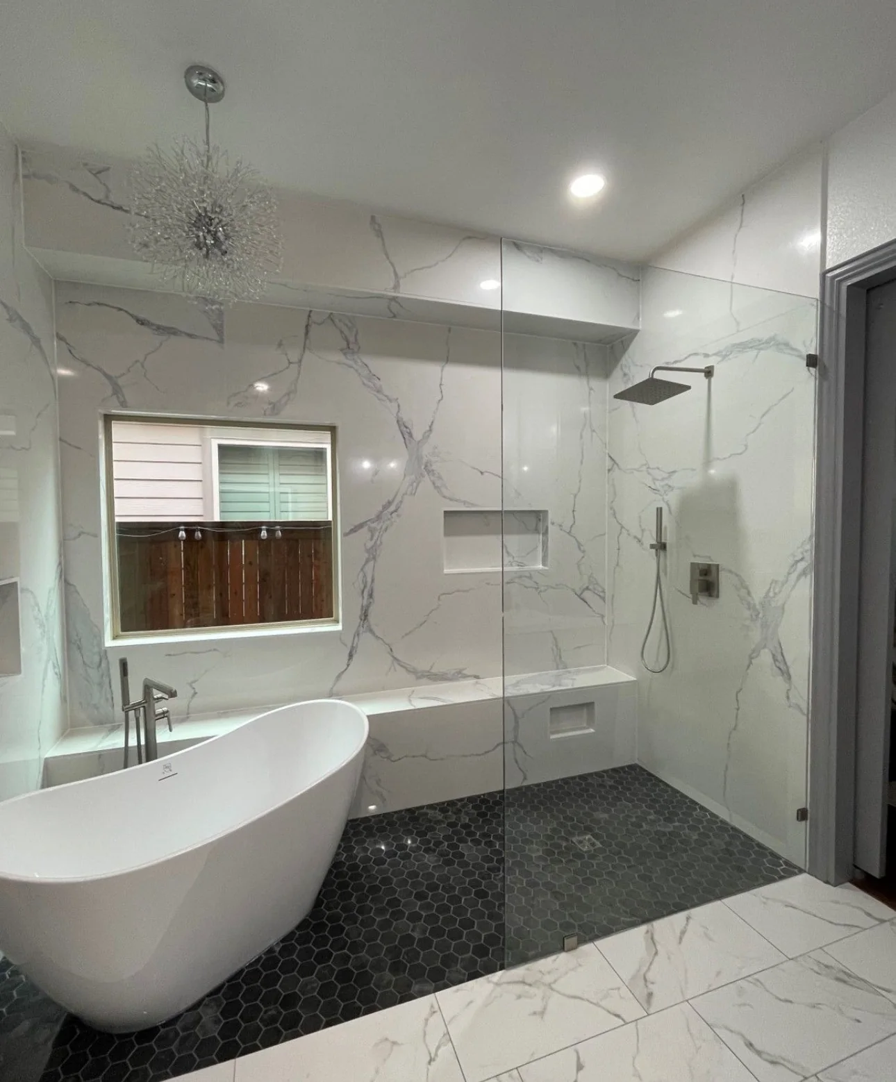 Enlarged wet area with zero-entry shower floor, freestanding tub, frameless glass, built-in bench, niches and marble-look walls